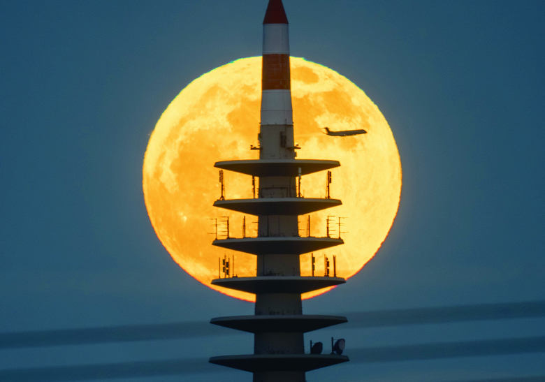23일 독일 프랑크푸르트의 TV 송전탑 뒤로 보름달이 뜨는 동안 여객기 한 대가 지나가고 있다. 뉴시스