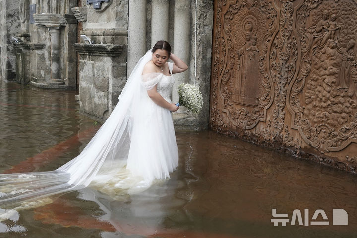 22일(현지 시간) 필리핀 불라칸주 말롤로스의 침수된 바라소아인 성당에서 신랑 베르디요와 결혼하는 신부 하마이카가 물 속에서 신부 입장을 준비하고 있다. 이 성당은 제6호 태풍 '위파'의 영향으로 침수돼 있었으나 신랑·신부는 결혼식을 강행했으며 하객들은 맨발에 바지를 걷어 올린 채 이들을 축하했다.  뉴시스